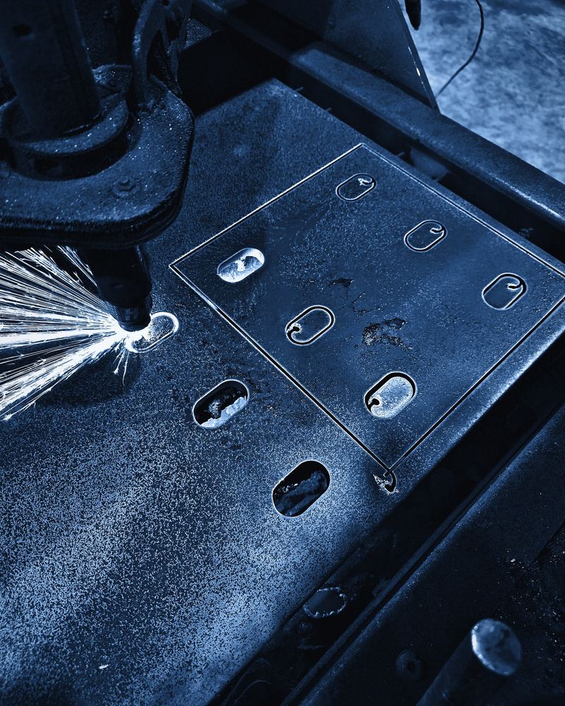 A plasma torch throws sparks while cutting slots in steel plate