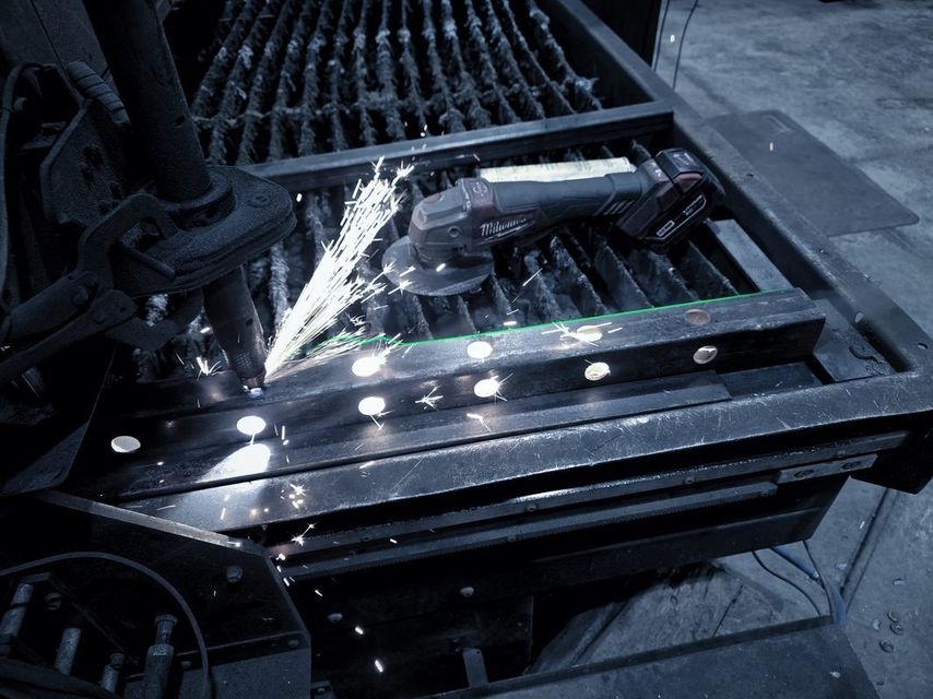 A grinder throws sparks across a cut part on the cutting table