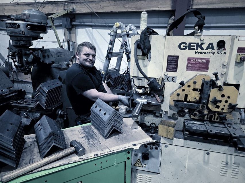 A man works at the ironworker with stacks of punched angle on the bench