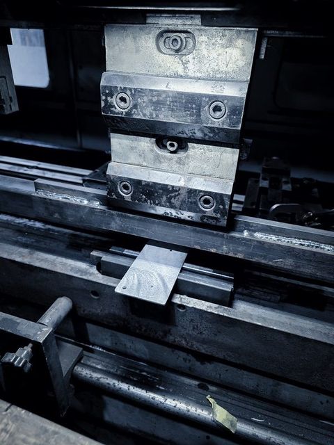 A small plate sits on the die of the press brake under the punch