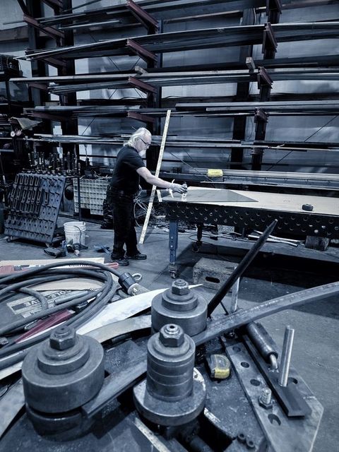 A bar curves through the roller while a man with white hair measures at the table behind