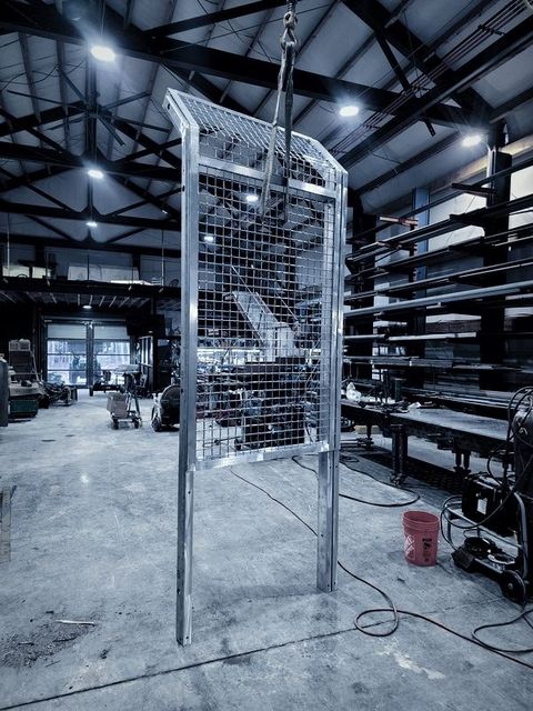 A framed wire mesh panel hangs from the hoist on the shop floor